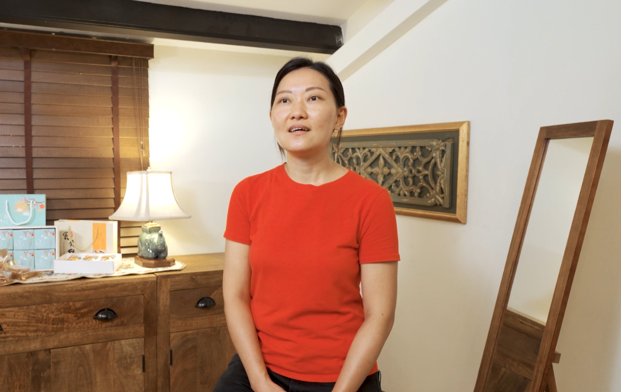 Lady in orange shirt sits in the middle of the room next to a cabinet.